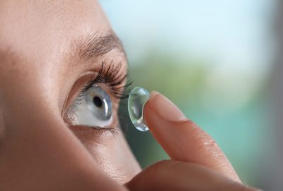 Young,Woman,Putting,Contact,Lens,In,Her,Eye,On,Blurred